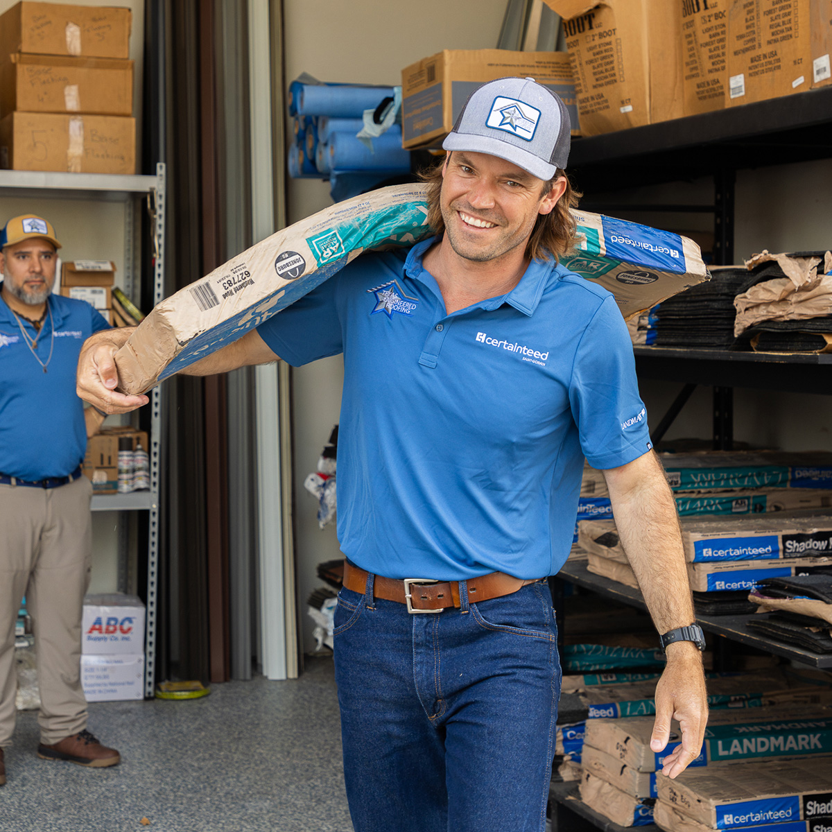 Smiling Texas Engineered Roofing team member carrying roofing materials on his shoulder in the warehouse