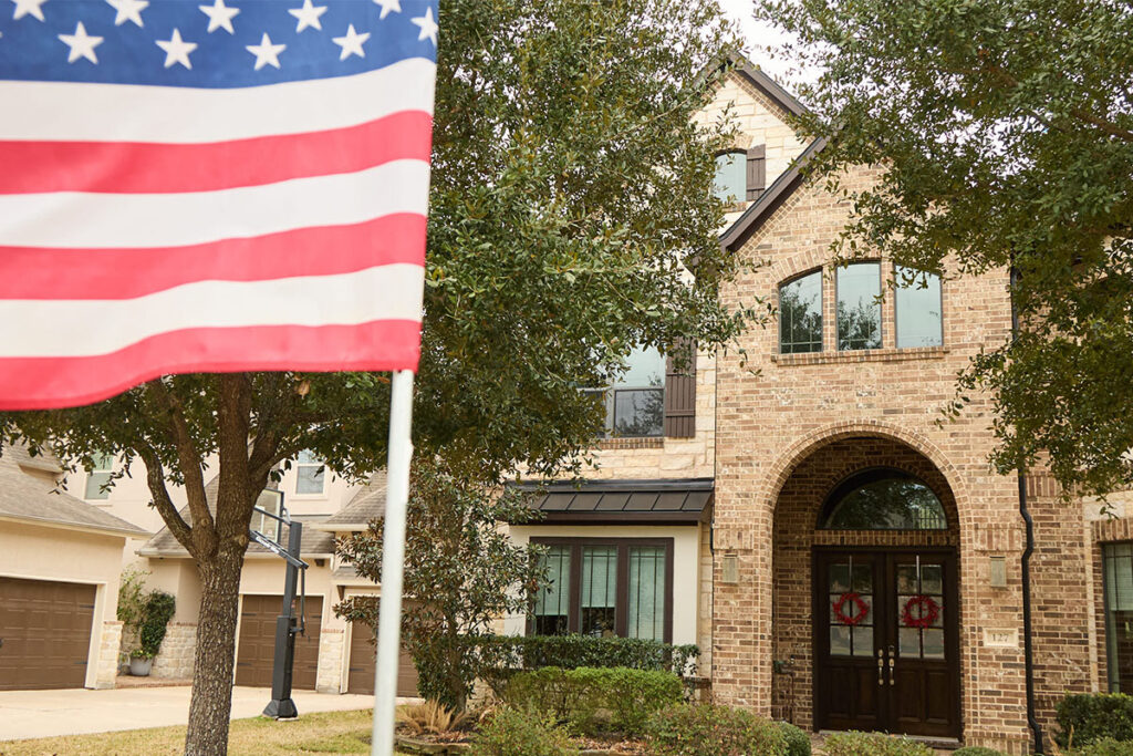 American flag flying in front of a two-story brick home with an arched entryway