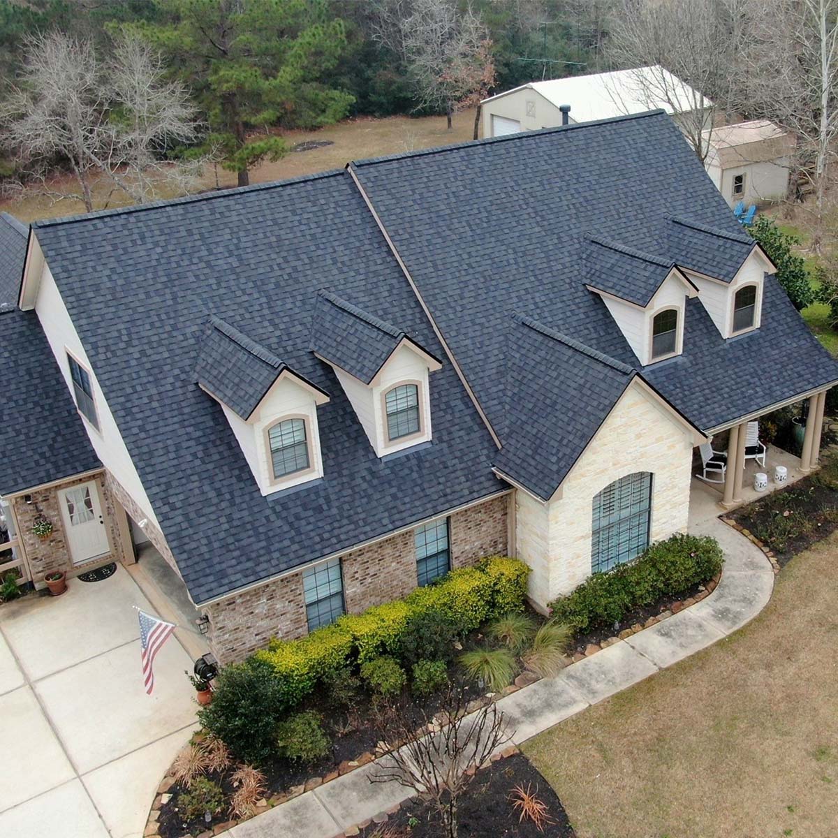 Brick and white home with a new charcoal shingle roof, three dormers, and a landscaped front yard