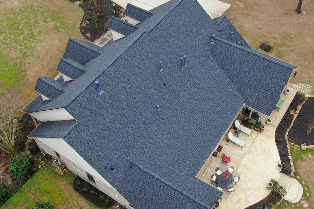 Aerial view of a single-story home with a charcoal shingle roof and a curved backyard patio