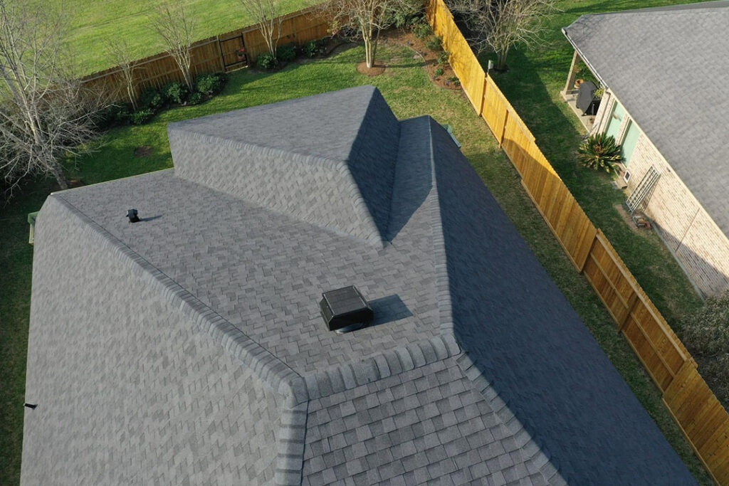 Gray shingle roof with a solar attic fan installed near the ridge, beside a wooden privacy fence
