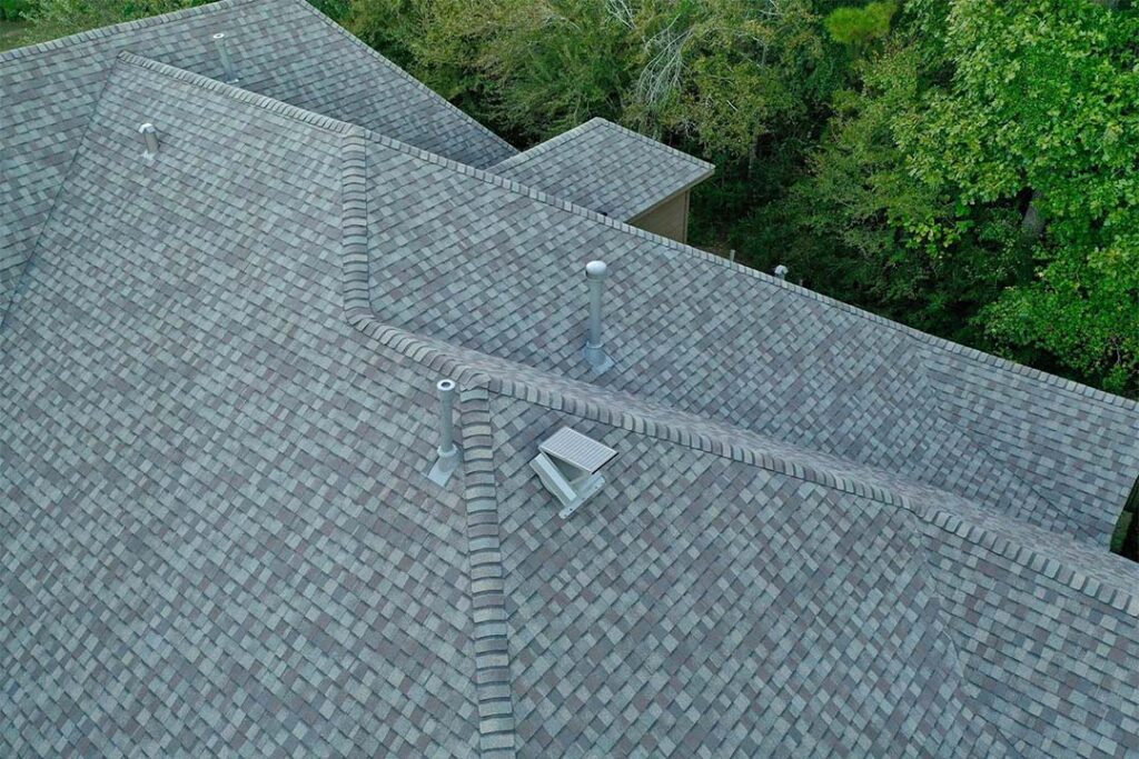 Attic Breeze solar attic fan installed on a gray architectural shingle roof surrounded by trees