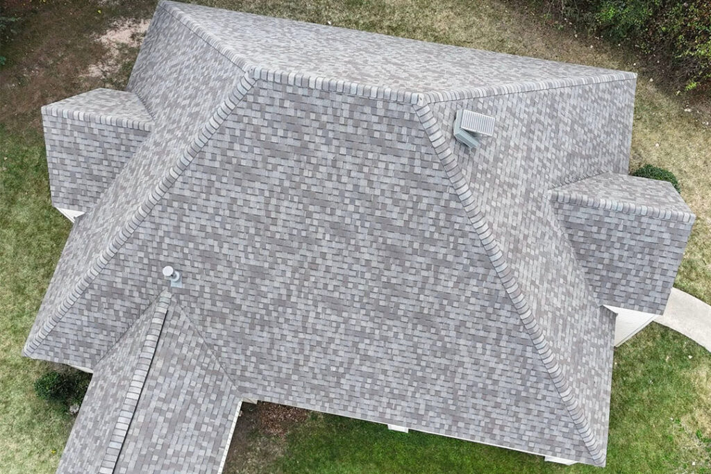 Aerial view of a gray shingle hip roof with a low-profile Attic Breeze solar attic fan installed