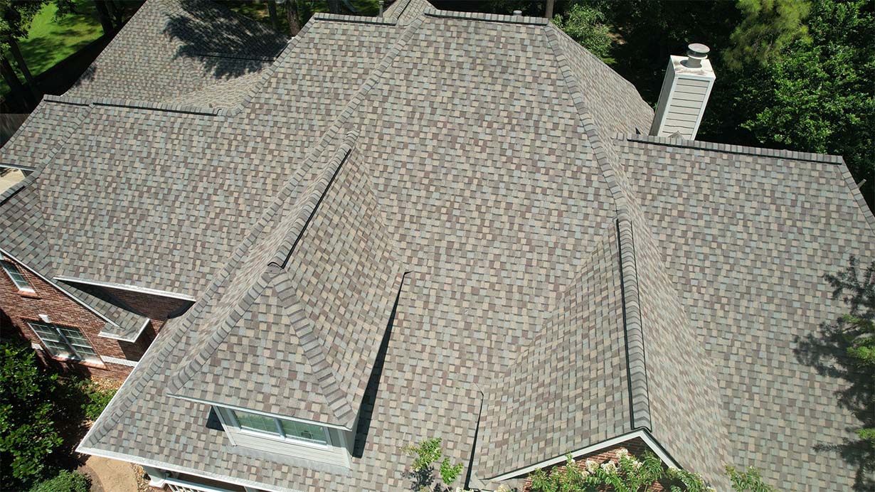 Aerial close-up of a gray architectural shingle roof with multiple hips, valleys, and a chimney