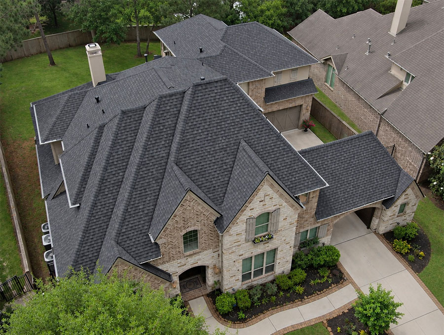 Aerial view of a two-story brick and stone home with a new charcoal architectural shingle roof