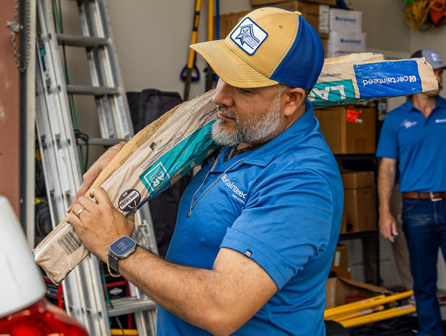 Roofer in a blue company shirt and cap carrying a roll of roofing underlayment on his shoulder in the warehouse