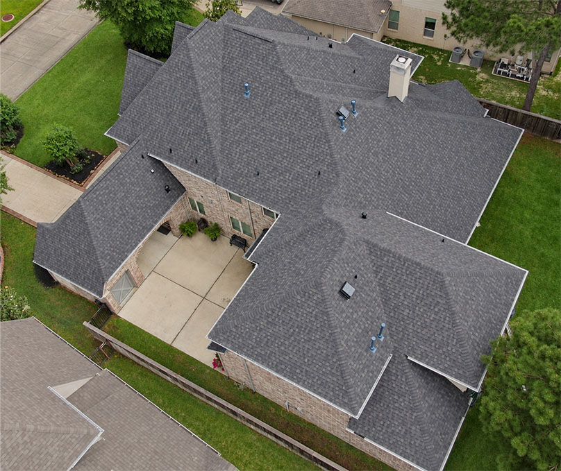 Aerial view of a gray asphalt shingle hip roof on a single-story home surrounded by a green lawn