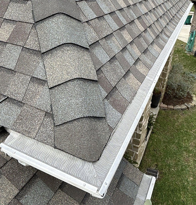 Close-up of architectural shingles along the roof edge above a white seamless gutter