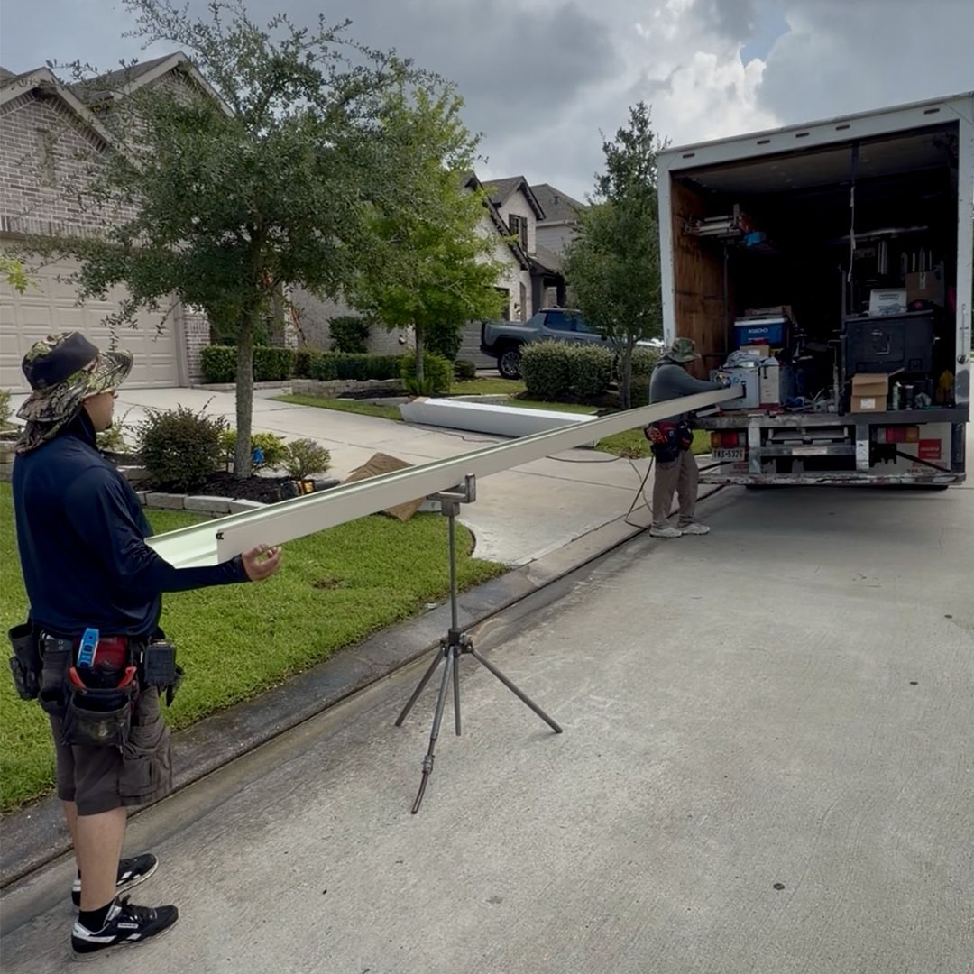 Gutter technician measuring a freshly formed seamless gutter beside the gutter machine truck in a driveway