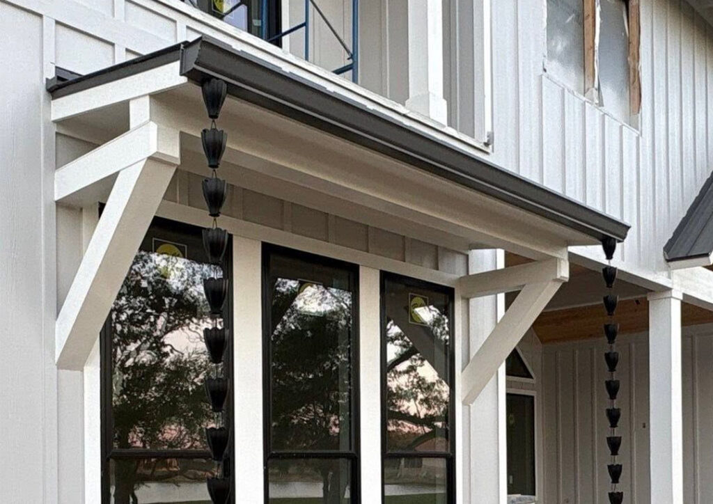 Black metal awning with gutters and rain chains on a white board-and-batten farmhouse exterior