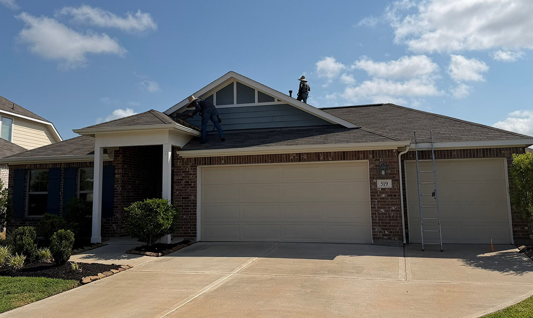 Single-story brick home with a gray shingle roof and a two-car garage under a blue sky