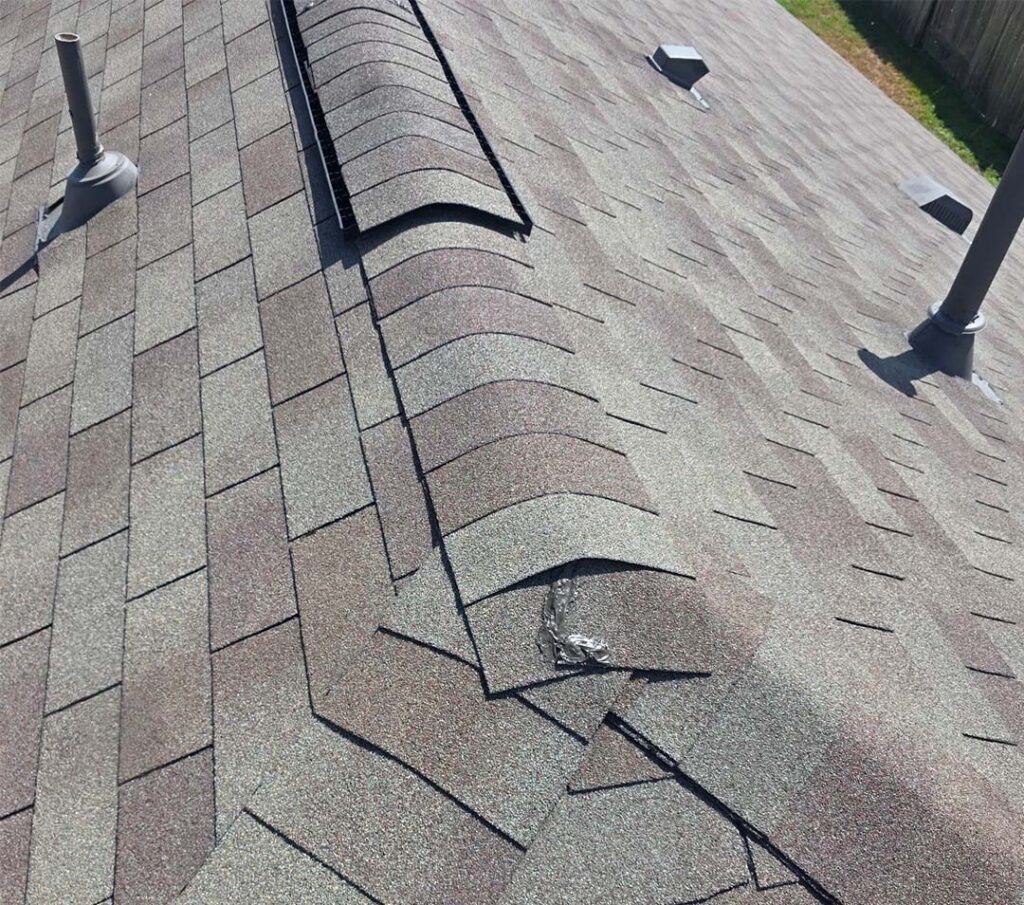Close-up of a new architectural shingle roof showing the ridge cap, vent, and pipe flashing