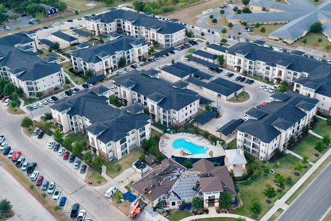 Aerial view of a large apartment complex with dark shingle roofs, a pool, and parking lots