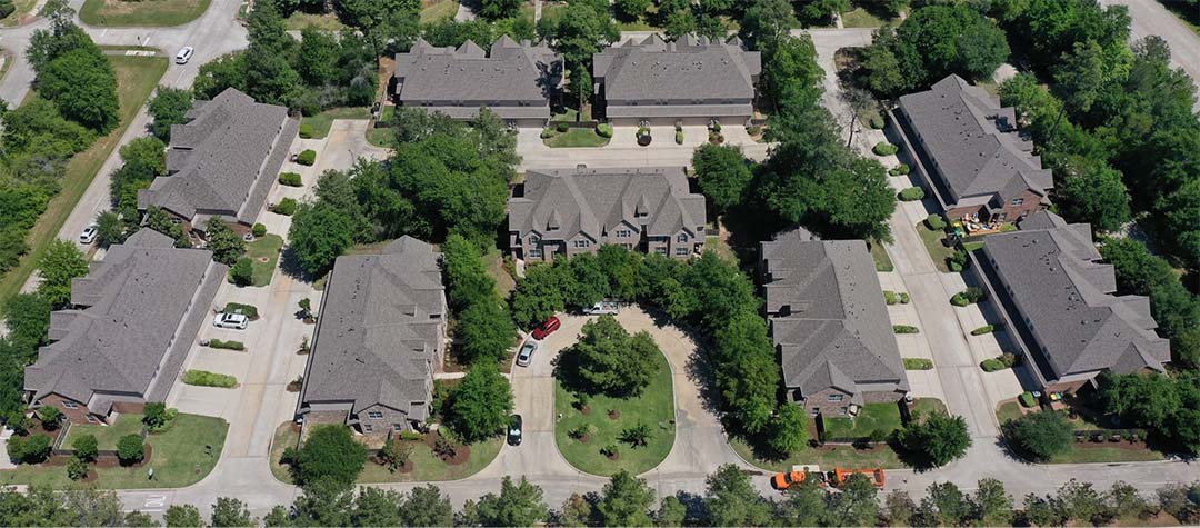 Aerial view of a townhome community with multiple gray shingle roofs and landscaped courtyards