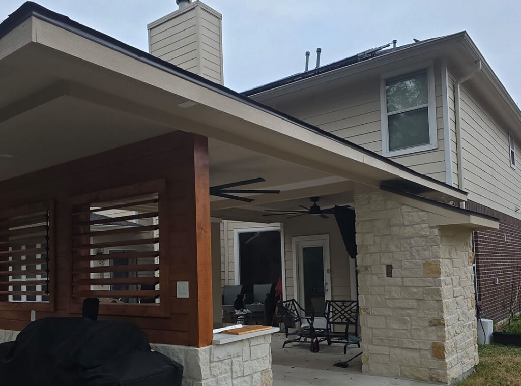 Modern covered patio extension with stone columns and wood slat accent walls on a two-story home
