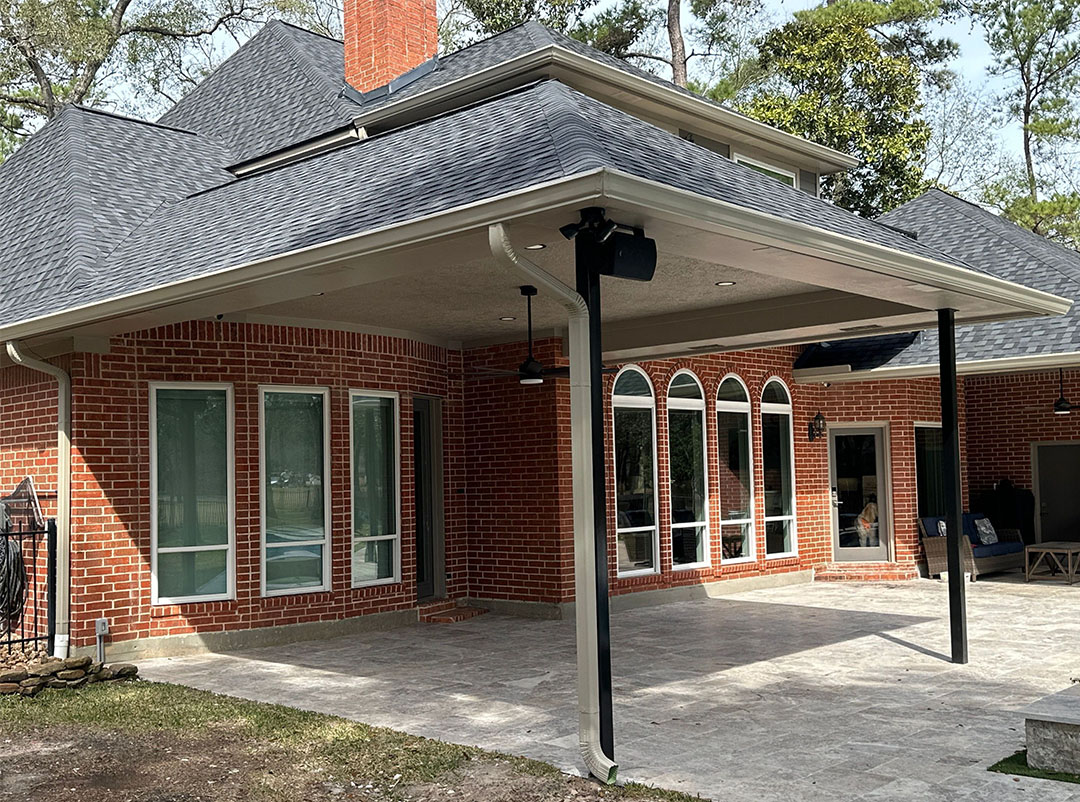 Large covered patio extension tied into the shingle roof of a brick home with a concrete slab