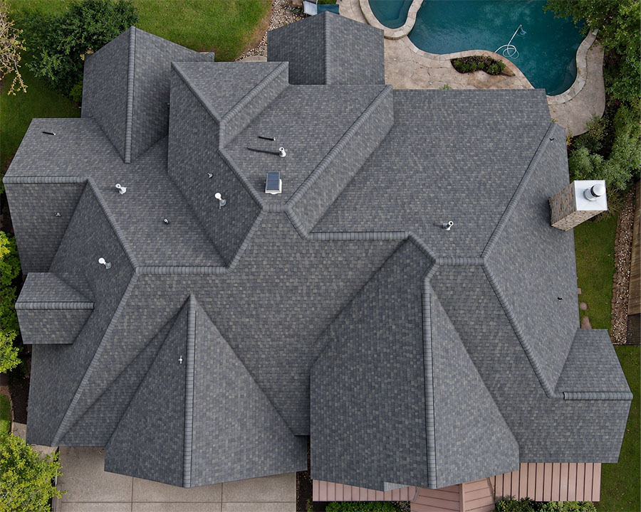 Aerial view of a complex dark gray shingle roof replacement on a large home next to a backyard pool