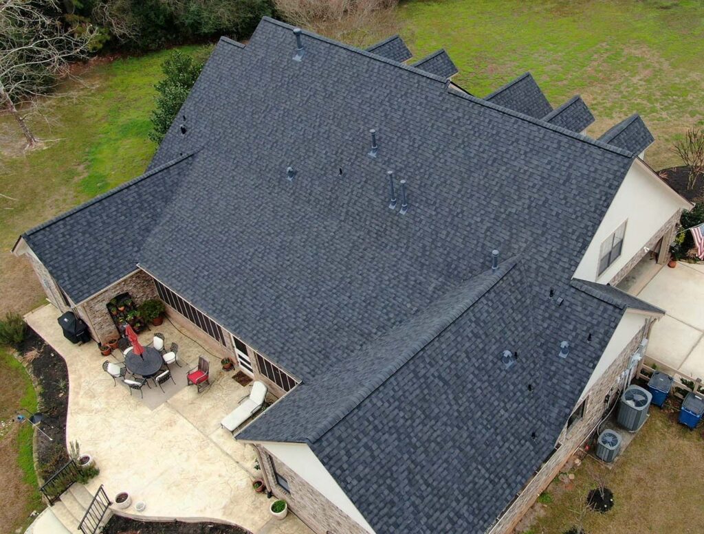 Aerial view of a single-story home with a new charcoal shingle roof and a backyard patio