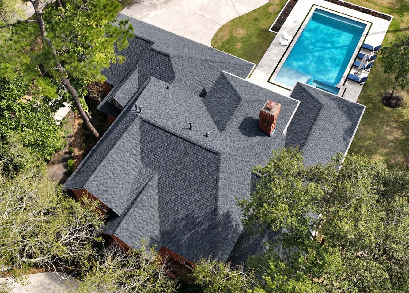 Aerial view of a residential charcoal shingle roof with a brick chimney beside a rectangular pool