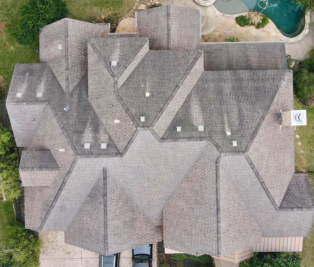 Aerial view of a finished gray shingle roof replacement on a large home with a backyard pool