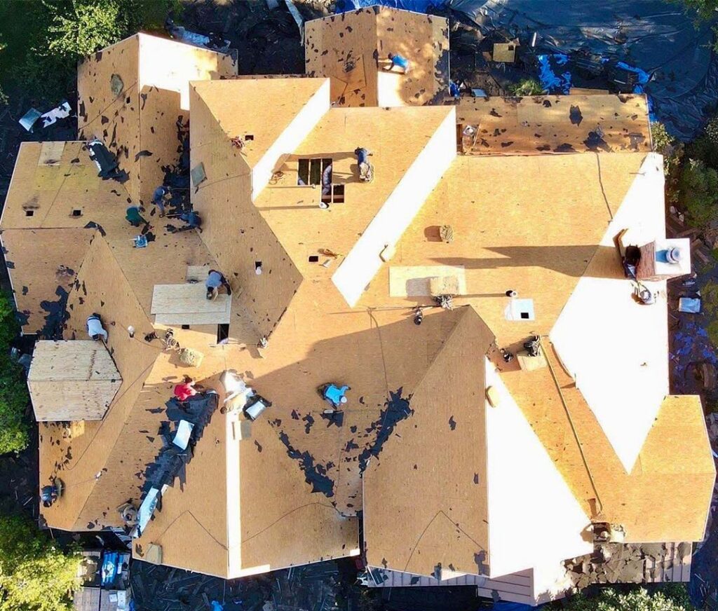 Aerial view of a roof replacement in progress with old shingles removed and wood decking exposed as the crew works