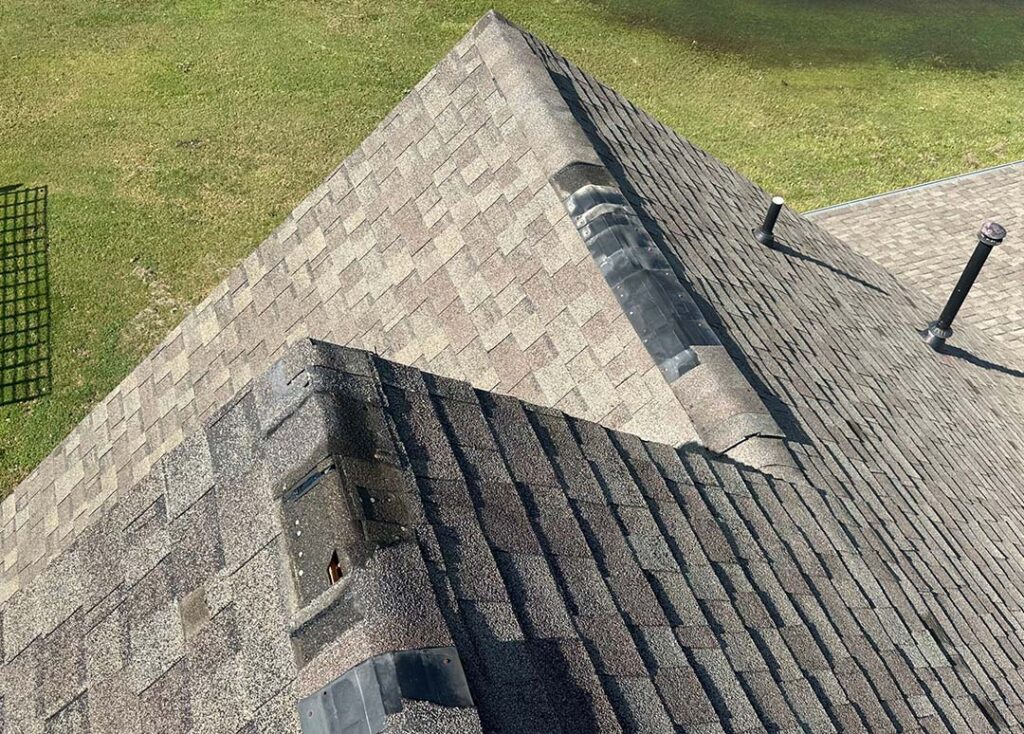 Roof ridge and hip section of a gray shingle roof being inspected for storm damage