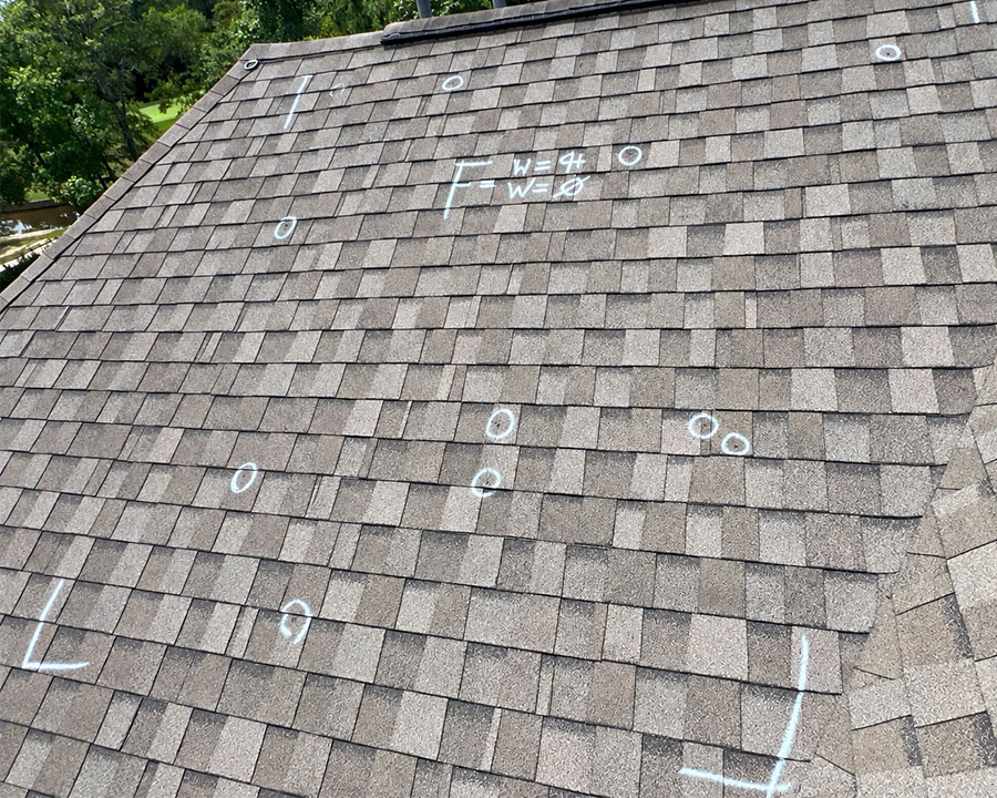 Shingle roof with chalk circles marking hail impact damage during a storm damage inspection