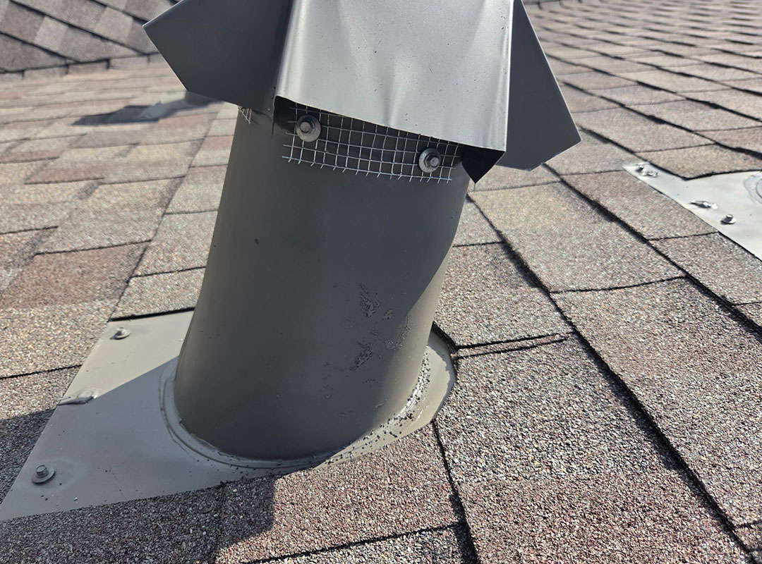Roof vent pipe fitted with a metal wildlife guard cap on a gray shingle roof